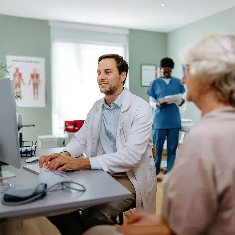 Young doctor working in office with senior woman as patient web