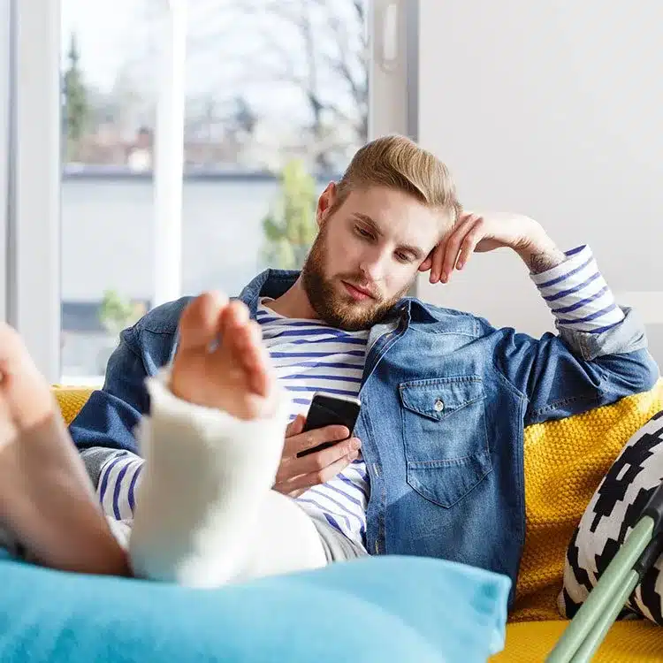 Young man with broken leg using smart phone at home web